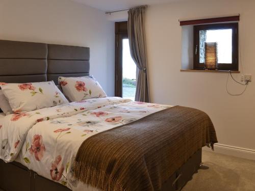 a bedroom with a bed with a floral comforter and a window at 1 Barnagh Barn in Kirkmichael