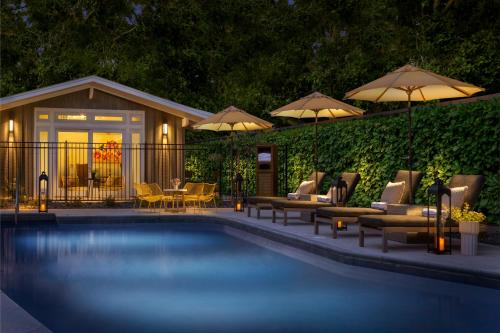 una piscina con sillas, mesas y sombrillas en The Cottages Hotel, en Menlo Park