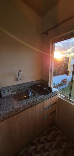 a kitchen with a sink and a window with the sunset at Pousada Campus Rosa in Praia do Rosa
