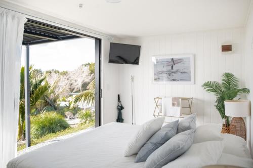 a white bedroom with a large bed and a large window at Aotearoa Surf Eco Pods in Te Arai
