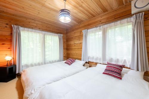 Dos camas en un dormitorio con paredes y ventanas de madera. en S-villa Karuizawa wood creek, en Tsumagoi