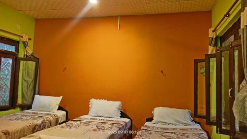 two beds in a room with an orange wall at Hotel Butterfly - Peaceful Garden for Nature Lovers in Sauraha