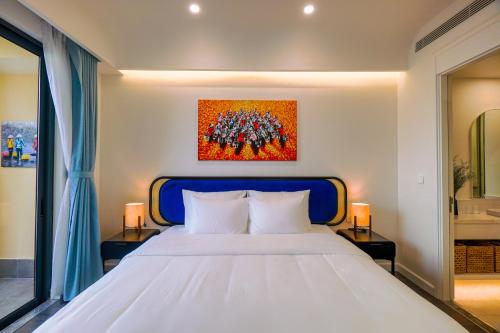 a bedroom with a white bed and a painting on the wall at Nexus House Ocean front & Hillside Phú Quốc in Phu Quoc