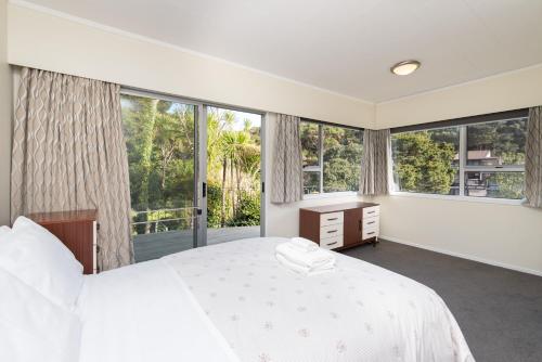 a bedroom with a white bed and large windows at Knights Retreat - Paihia Holiday Home in Paihia
