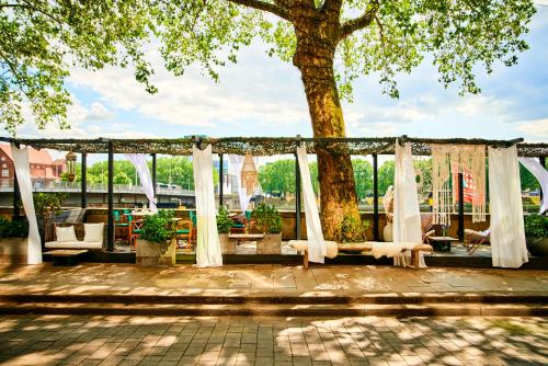 an outdoor patio with white curtains and a tree at Designhotel ÜberFluss in Bremen