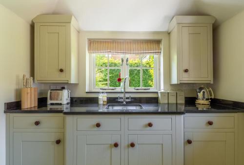 a kitchen with white cabinets and a sink and a window at Hope Cottage - West Sussex in Henfield