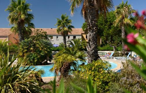 un complexe avec une piscine et des palmiers dans l'établissement Résidence Odalys Le Grand Bleu, à Vendres-Plage