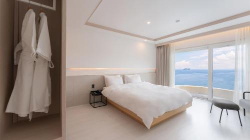 a bedroom with a white bed and a large window at Geoje Mongdol Beach H Avenue Hotel in Geoje 