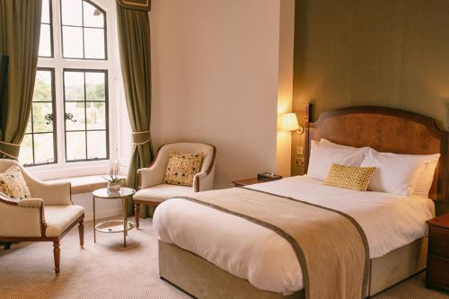 ファーンバラにあるThe Elvetham Hotelの大きなベッドと椅子2脚が備わるホテルルームです。