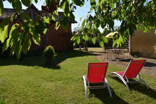 deux chaises rouges assises dans l'herbe sous un arbre dans l'établissement Du vert & du bon air - Linge maison inclus - Parking Privé Gratuit - Centre ville Bergerac 10mn - Domaine Bellevue Cottage en Périgord, à Lembras