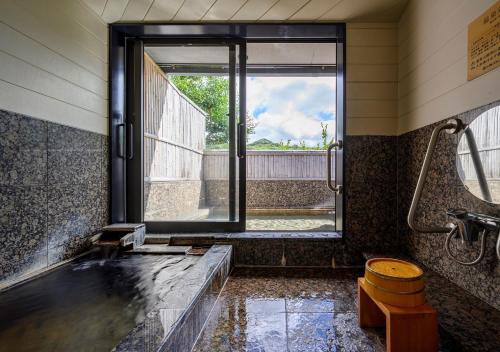 a bathroom with a shower and a tub with a window at Kawatana Grand Hotel Otafuku in Shimonoseki