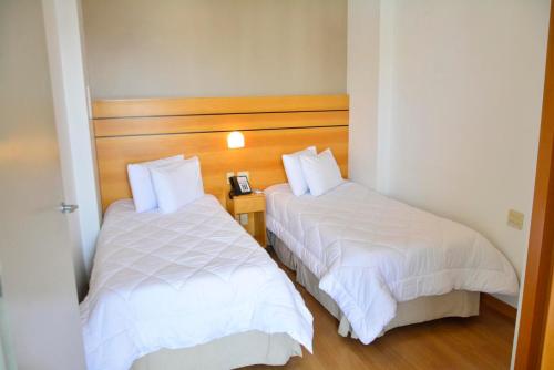 duas camas num quarto de hotel com lençóis brancos em San Diego Suítes Lourdes - OFICIAL em Belo Horizonte