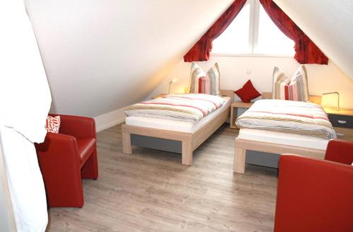 two beds in a attic room with red chairs at Mien Dröm in Norddeich