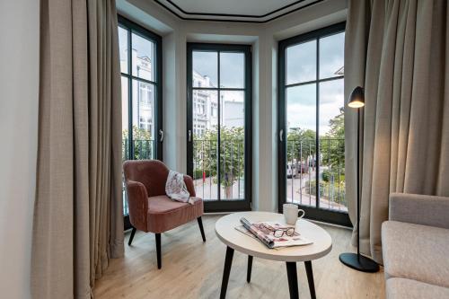 een woonkamer met een tafel, een stoel en ramen bij Gustav Appartements in Binz