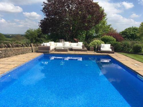 a large blue swimming pool with couches at Harcombe Barn near Bristol in Bristol