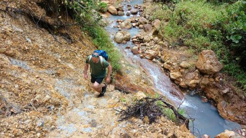 a man walking down a rocky trail next to a river at Cozy vacation retreat with free parking in Roseau