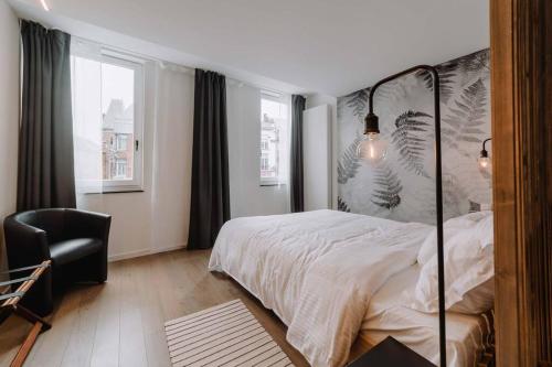 a bedroom with a bed and a chair and windows at Chimay : La Chambre Bleue de la Grand Place in Chimay