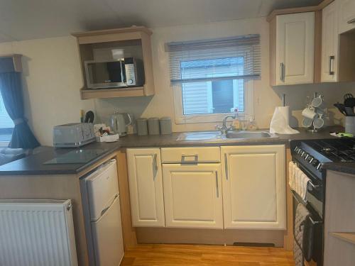 a kitchen with white cabinets and a sink and a stove at 3 Bedroom Caravan - Maples 126, Trecco Bay in Newton