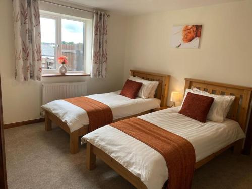 two beds in a hotel room with a window at Bungalow in Pillaton in Saltash