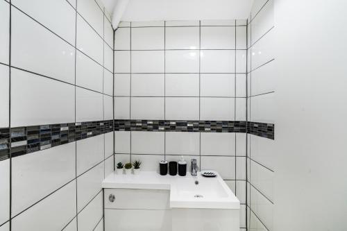 ein weiß gefliestes Bad mit einem weißen Waschbecken in der Unterkunft Exquisite London Home - Parking - Sleeps 10 in Dagenham