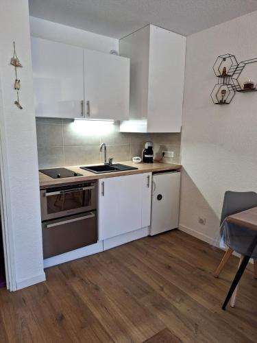 - une cuisine avec des placards blancs, un évier et une table dans l'établissement Studio Les 3 Lys Auron, à Auron