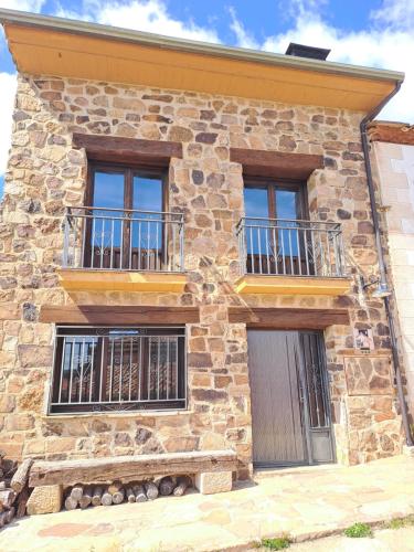 a stone house with three windows and a balcony at La Fragua I y II in Rebollar