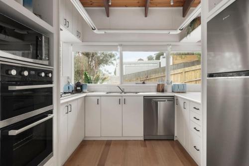 a kitchen with white cabinets and a large window at Surfcoast Soul - Stylish Dog Friendly Retreat - Torquay in Torquay