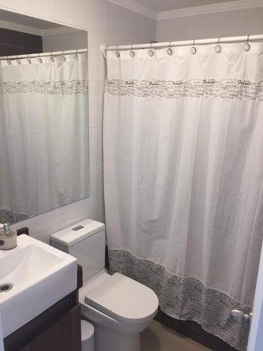 a bathroom with a white toilet and a shower curtain at Acogedor departamento a pasos de la playa in Coquimbo