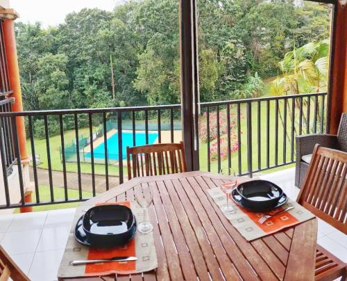 una mesa de madera en un balcón con vistas a la piscina en Appartement cosy dans résidence avec piscine, en Fort-de-France