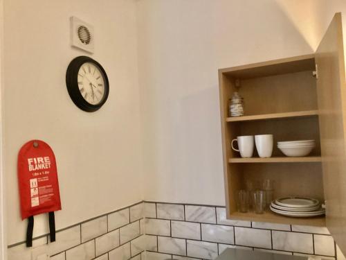 a clock on a wall next to a shelf with dishes at Coventry Train station studio in Coventry