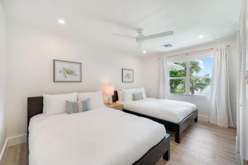 two beds in a white room with a window at Renovated, Oceanfront 2bd Seven Mile Beach Condo with amazing views in George Town
