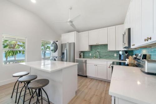 a white kitchen with white cabinets and stools in it at Renovated, Oceanfront 2bd Seven Mile Beach Condo with amazing views in George Town