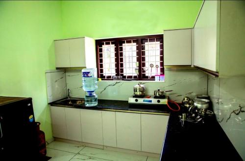 cocina con paredes verdes, armarios blancos y ventana en DREAMS VILLA Near Rajagiri Hospital, en Alwaye