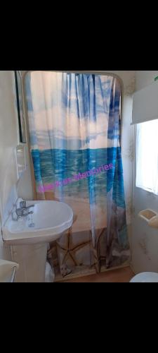 a bathroom with a sink and a shower curtain at Mackies Memories. in Hemsby