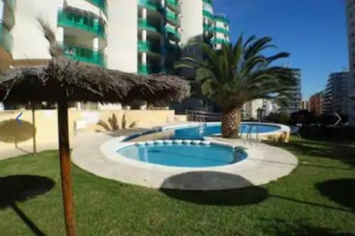 een zwembad met een palmboom en een gebouw bij Precioso apartamento en complejo residencial con piscina,barbacoa y pista de padel. in Villajoyosa
