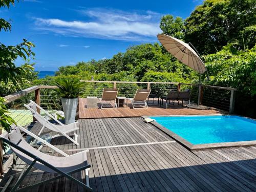 eine Terrasse mit einem Pool, Stühlen und einem Sonnenschirm in der Unterkunft Case Coco Pointe Batterie. Piscine, vue mer, 4 p. in Deshaies