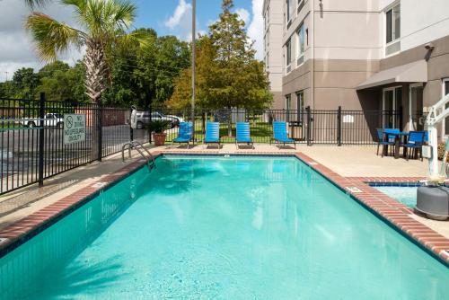 a swimming pool with blue chairs and a building at Hilton Garden Inn Baton Rouge Airport in Baton Rouge