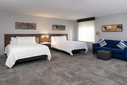 Habitación de hotel con 2 camas y sofá azul en Hilton Garden Inn Baton Rouge Airport en Baton Rouge