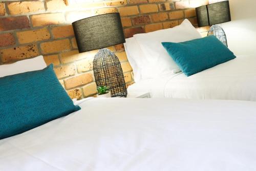 two white beds with blue pillows next to a brick wall at Kennedy Drive Boutique Motel - Close To City Centre & Airport in Tweed Heads