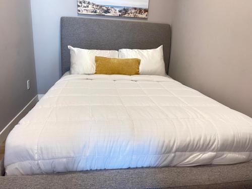 a large white bed with a yellow pillow on it at Cozy basement suite in Calgary