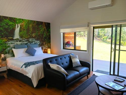 a bedroom with a bed and a leather couch at Hideaway Falls - Staggys Cottage in Mapleton