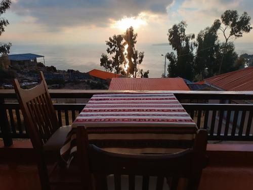 a table and chairs on a balcony with the sun setting at Hostal Quilla Wasi Isla del Sol in Comunidad Yumani