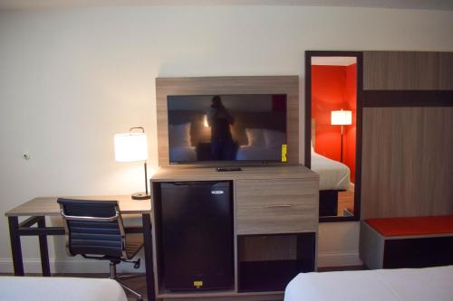 a hotel room with a television and a desk with a bed at Ramada by Wyndham Cleveland Airport West in Fairview Park