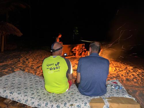 Juani beach bungalows في كيليندوني: رجلان يجلسان على الشاطئ يشاهدان النار