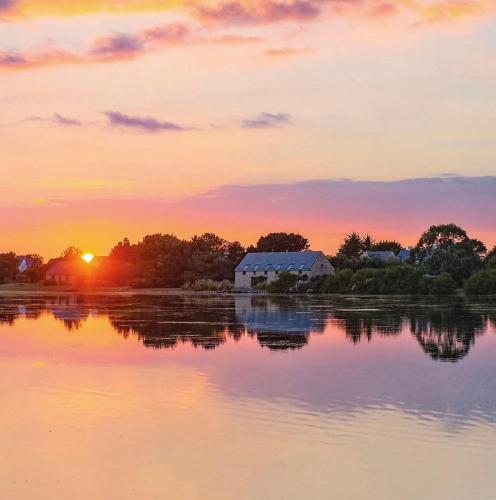 a barn on the shore of a lake at sunset at Appart'Hôtel & Spa "Les Voiles" Le Batz in Carnac