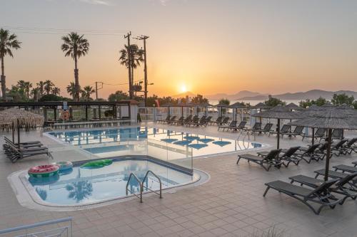 een zwembad in een resort met een zonsondergang op de achtergrond bij Akti Dimis Hotel in Tigaki