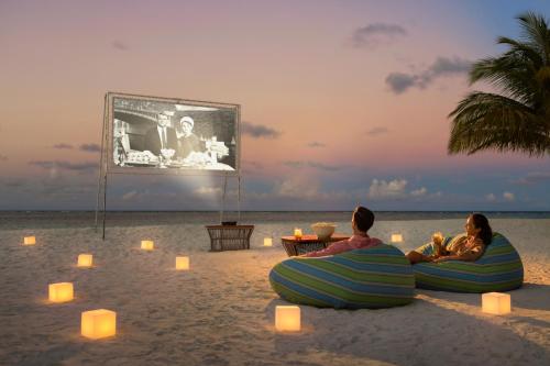 two people sitting on the beach watching a movie at Angsana Velavaru in Dhaalu Atoll