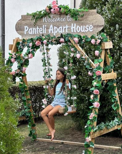 a girl sitting on a bench under a garden arch with roses at PANTELI APART HOUSE in Aheloy