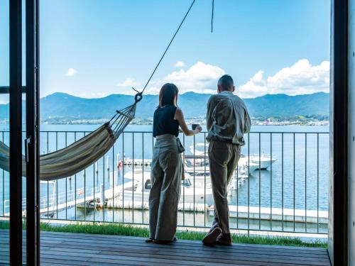 a man and a woman standing in a hammock overlooking the water at YANMAR SUNSET MARINA CLUBHOUSE&HOTEL in Moriyama