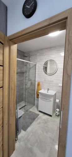 ein Badezimmer mit einer Dusche, einem Waschbecken und einer Uhr in der Unterkunft Apartament Bursztyn in Jantar